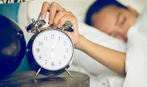 Alarm clock beside a person using a sleep hygiene checklist to improve sleep habits